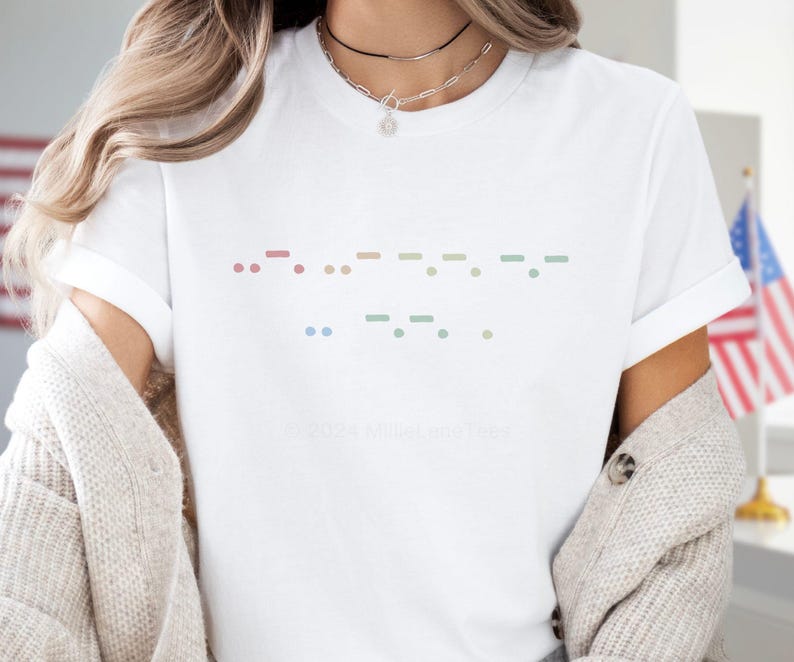 May include: White t-shirt with a Morse code design in pastel colors. The design features dots and dashes arranged in a horizontal pattern. The text "&copy; 2024 MilltownTees" is printed at the bottom of the shirt.