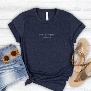 Peut inclure: T-shirt bleu marine avec l'inscription blanche "Don't be a jerk. -[Jesus]" . Le t-shirt est associ&eacute; &agrave; un short en jean, des lunettes de soleil orange et des sandales dor&eacute;es.
