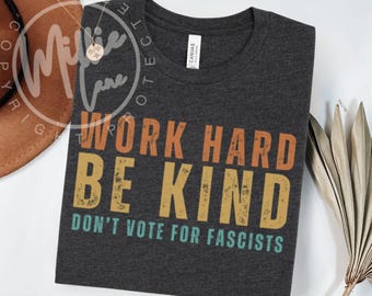 May include: Dark gray t-shirt with the text "WORK HARD BE KIND DON'T VOTE FOR FASCISTS" in orange, yellow, and teal. The shirt is made of a soft material and is a crew neck style.
