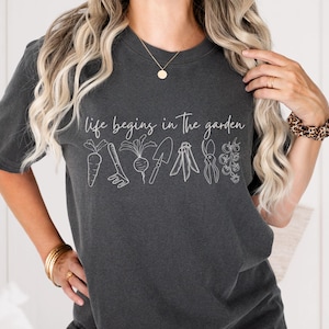 May include: A dark grey t-shirt with the text "life begins in the garden" and a line drawing of gardening tools and vegetables.