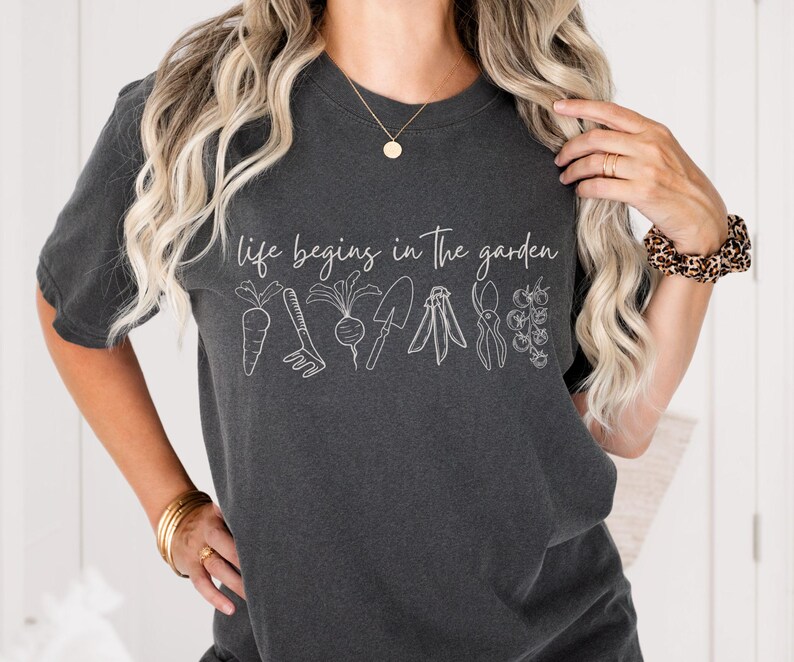 May include: A dark grey t-shirt with the text "life begins in the garden" and a line drawing of gardening tools and vegetables.