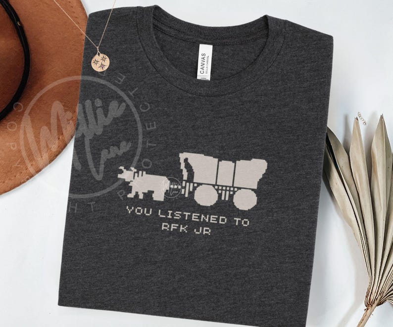 Puede incluir: Camiseta gris oscuro con un oso pixelado tirando de una carreta cubierta. El texto "YOU LISTENED TO RFK JR" est&aacute; debajo del gr&aacute;fico. La camiseta est&aacute; hecha de un material suave.