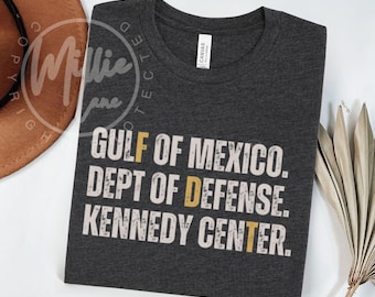 Könnte beinhalten: Dunkelgraues T-Shirt mit dem Text "GULF OF MEXICO. DEPT OF DEFENSE. KENNEDY CENTER." in verblichener weißer Schrift mit gelben Akzenten. Das Shirt besteht aus einem weichen Material.
