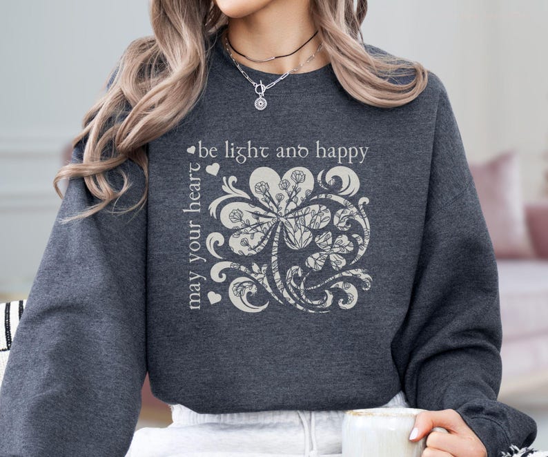 May include: A dark gray sweatshirt with a white graphic of a stylized four-leaf clover with the text "may your heart be light and happy".