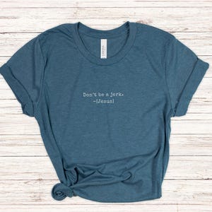 Peut inclure: T-shirt bleu sarcelle avec des manches retrouss&eacute;es. Le texte "Don't be a jerk. -[Jesus]" est imprim&eacute; en blanc. Le t-shirt est en mati&egrave;re souple et nou&eacute; en bas. V&ecirc;tement d&eacute;contract&eacute;.