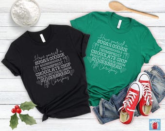 Pode incluir: Duas camisetas pretas e verdes com um design branco que diz "Have yourself a Sugar Cookie, Snickerdoodle, Thumbprint, Chocolate Chip, Peanut Butter Blossom, Gingerbread, Merry Christmas".