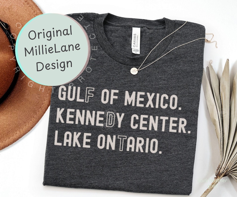 May include: A dark charcoal heather gray t-shirt with a crew neckline and a white graphic print that reads GULF OF MEXICO. KENNEDY CENTER. LAKE ONTARIO. The shirt features a white brand label at the inner neck and a thin silver chain necklace.