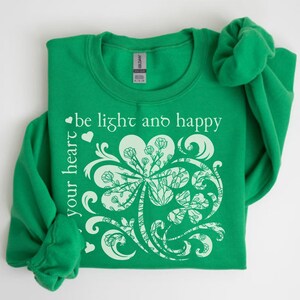 May include: Green sweatshirt with a white shamrock design and the text "be light and happy your heart".