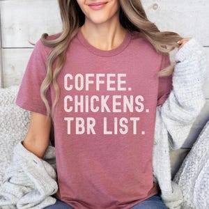 May include: A heather pink t-shirt with the text "COFFEE. CHICKENS. TBR LIST." in white lettering.