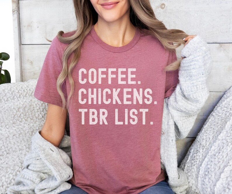 May include: A heather pink t-shirt with the text "COFFEE. CHICKENS. TBR LIST." in white lettering.