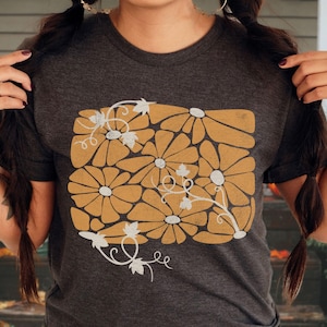 May include: A dark gray t-shirt with a graphic print of stylized yellow flowers and white vines.