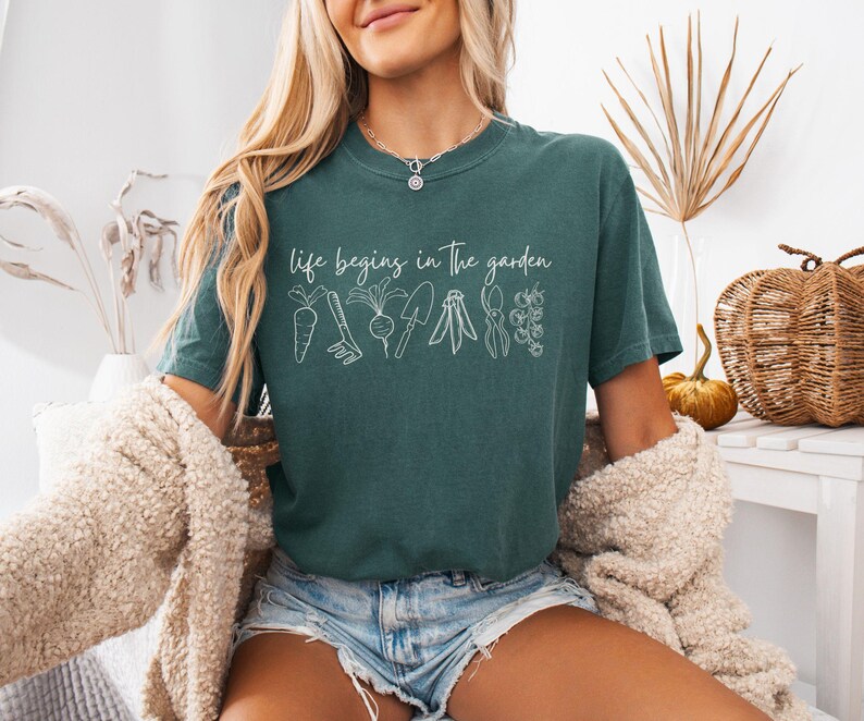 May include: A teal blue t-shirt with the text "life begins in the garden" and a white outline of gardening tools and plants.