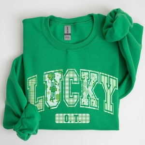 May include: Green sweatshirt with a white and green "LUCKY O.T." graphic. The letters are made of a patchwork of green shamrocks, white gingham, and white floral patterns.