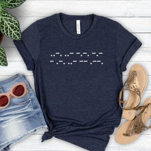 May include: A navy blue t-shirt with a white design of the word "LOVE" written in braille.