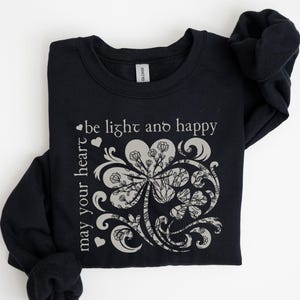 May include: Black sweatshirt with a white graphic of a stylized four-leaf clover with the text "may your heart be light and happy".