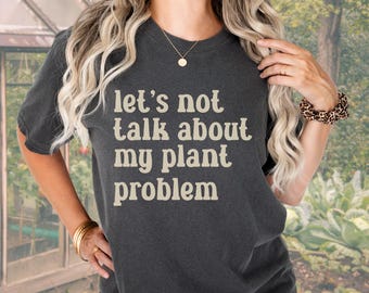 Peut inclure: Un t-shirt gris foncé avec le texte "Let's not talk about my plant problem" imprimé en beige clair.