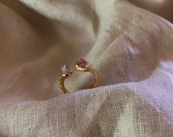 May include: Gold ring with two stones, one white and one pink, set in a textured gold band.