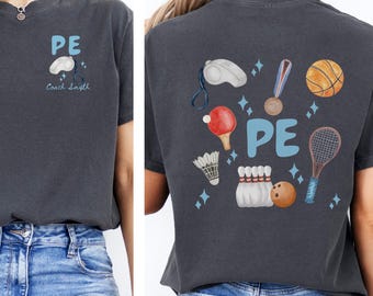 May include: Dark gray t-shirt with "PE" in light blue and sports-themed illustrations. The front has "PE" and a coach's whistle graphic. The back features a whistle, medal, basketball, and other sports equipment.