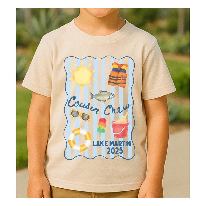 May include: A beige t-shirt featuring a colorful graphic with the text "Cousin Crew Lake Martin 2025." The graphic includes a sun, life vest, fish, sunglasses, popsicle, sand pail, and a life preserver. The shirt is short-sleeved.