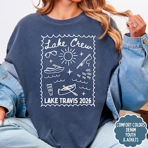 May include: A navy blue sweatshirt with a white graphic that reads "Lake Crew" and "Lake Travis 2026". The graphic includes illustrations of sunglasses, a sun, a jet ski, fish, a fishing rod, a boat, and sunscreen.