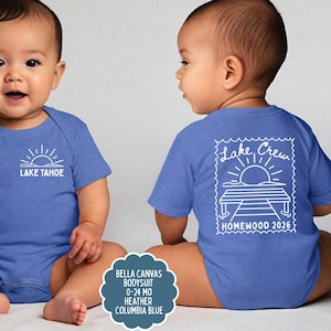 May include: A heather Columbia blue baby bodysuit featuring a white graphic of a sun over Lake Tahoe on the front and a larger white graphic of a sun over a dock with the text Lake Crew HOMEWOOD 2026 on the back, sized for 0-24 months.