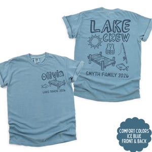 May include: Two ice blue t-shirts. One shirt has "Olivia" and "LAKE TAHOE 2026" printed on the front. The other shirt has "LAKE CREW" and "SMYTH FAMILY 2026" printed on the back, with lake-themed graphics. The shirts are Comfort Colors.