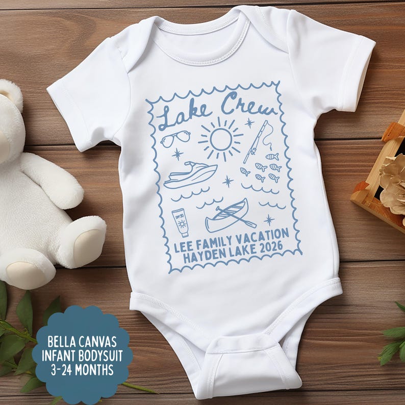 May include: White infant bodysuit with a blue "Lake Crew" design featuring sunglasses, a sun, a jet ski, fish, and a canoe. The text "LEE FAMILY VACATION HAYDEN LAKE 2026" is also included. The bodysuit is sized for 3-24 months.