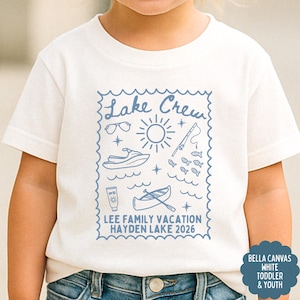 May include: White toddler t-shirt with a blue graphic that reads "Lake Crew" with illustrations of sunglasses, a sun, a jet ski, fish, sunscreen, and a canoe. The text "LEE FAMILY VACATION HAYDEN LAKE 2026" is also included.