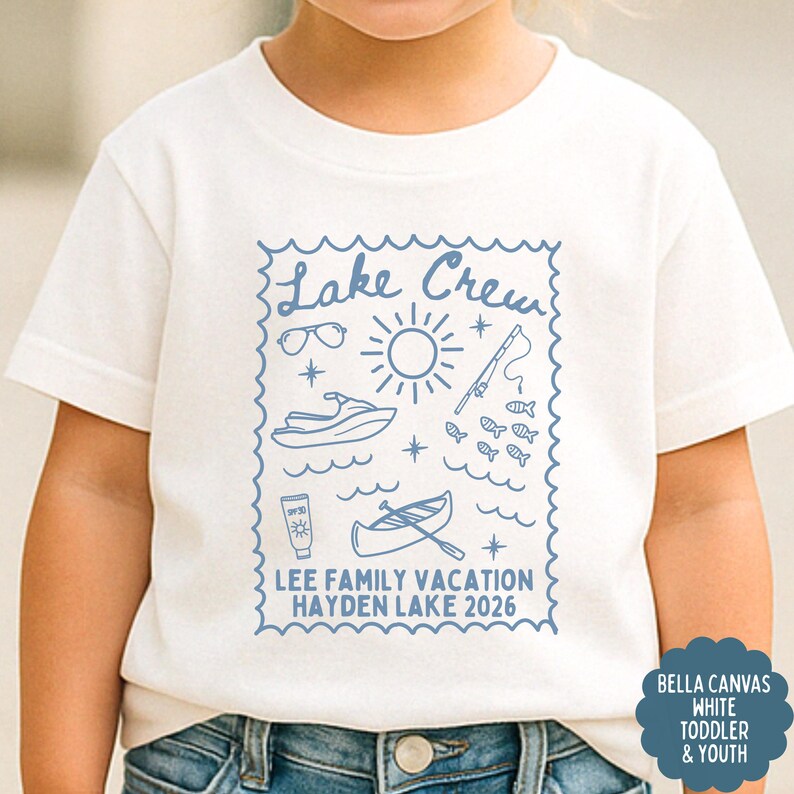 May include: White toddler t-shirt with a blue graphic that reads "Lake Crew" with illustrations of sunglasses, a sun, a jet ski, fish, sunscreen, and a canoe. The text "LEE FAMILY VACATION HAYDEN LAKE 2026" is also included.