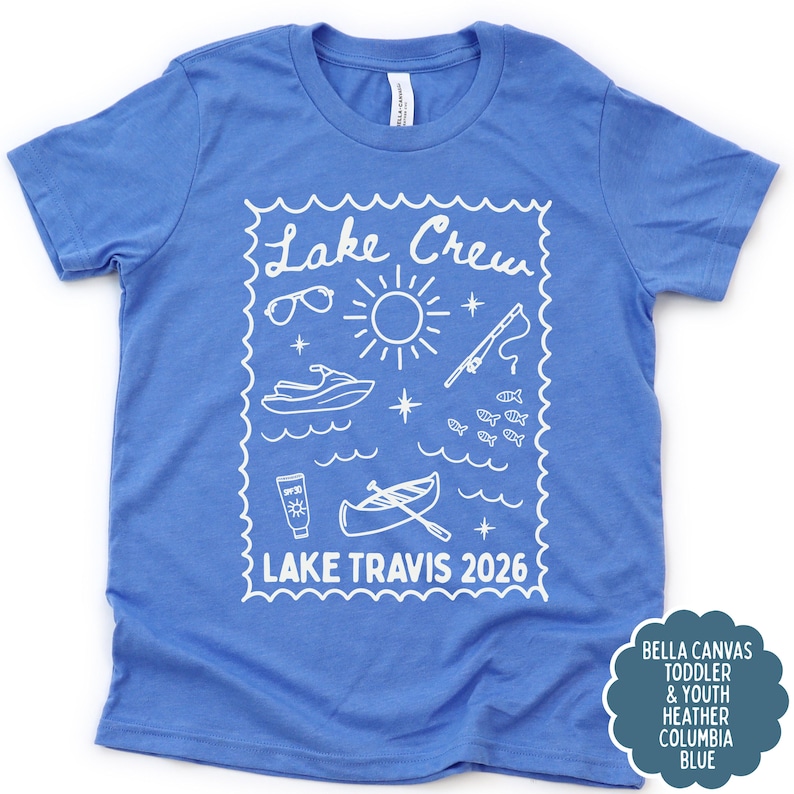 May include: A blue t-shirt with a white graphic design featuring the words "Lake Crew" and "Lake Travis 2026." The design includes illustrations of sunglasses, a sun, a jet ski, a fishing rod, fish, sunscreen, and a boat.