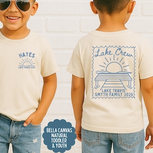 May include: A natural-coloured t-shirt featuring a blue graphic print. The front displays the name Hayes above a sun icon and Lake Travis 2026. The back shows a large stamp-shaped design with a sun, dock, and the text Lake Crew Lake Travis Smyth Family 2026.