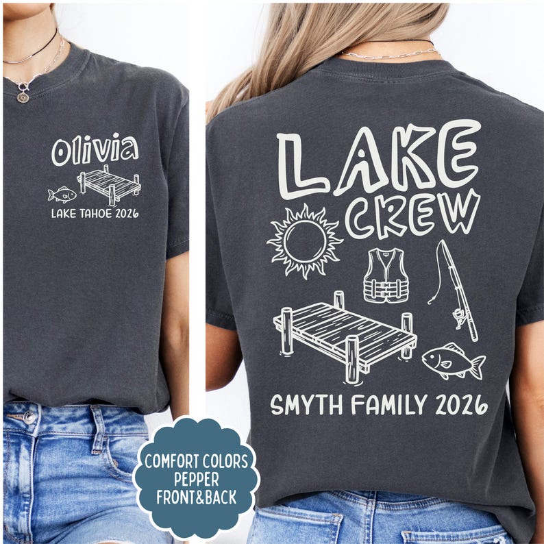 May include: Dark gray t-shirt with white graphic designs. The front features the name "Olivia", a fish, and a dock, with "LAKE TAHOE 2026" below. The back displays "LAKE CREW", a sun, life vest, fishing rod, dock, fish, and "SMYTH FAMILY 2026".