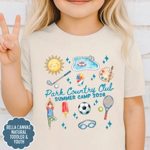 K&ouml;nnte beinhalten: Beiges Bella Canvas T-Shirt f&uuml;r Kleinkinder und Jugendliche mit einem farbenfrohen Sommercamp-Motiv. Das Design umfasst eine Sonne, einen Pool, einen Golfschl&auml;ger, Eis, einen Fu&szlig;ball und einen Tennisschl&auml;ger. Der Text lautet "Park Country Club Summer Camp 2026."