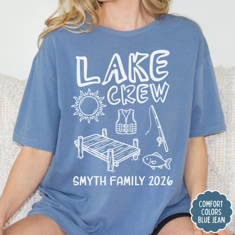 May include: Blue jean colored t-shirt with the words "LAKE CREW" and lake-themed graphics in white. The graphics include a sun, life vest, fishing pole, dock, and fish. The text "SMYTH FAMILY 2026" is printed below the graphics.