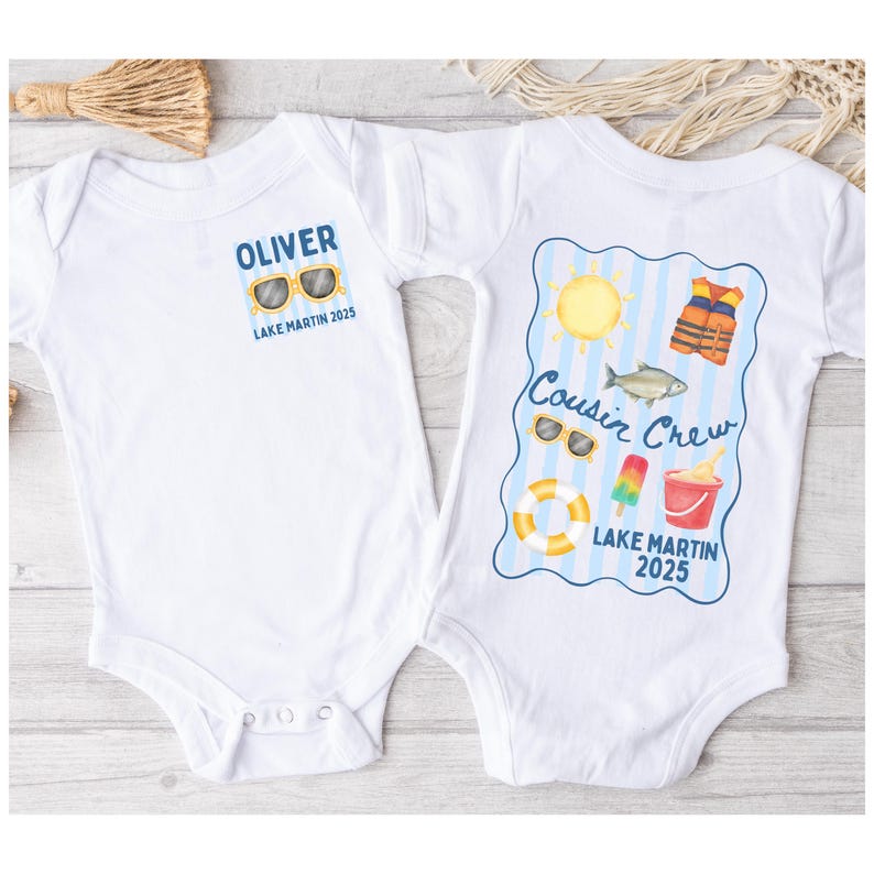 May include: Two white baby onesies. One has "OLIVER" above sunglasses and "Lake Martin 2025". The other has "Cousin Crew" above a sun, fish, life vest, sunglasses, popsicle, bucket, and life preserver, with "Lake Martin 2025".