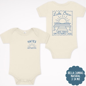 May include: Two natural-coloured baby bodysuits with short sleeves. The left bodysuit features a small blue graphic of a sun and the text "HAYES LAKE TRAVIS 2026". The right bodysuit displays a large blue stamp-style graphic of a dock and sun.
