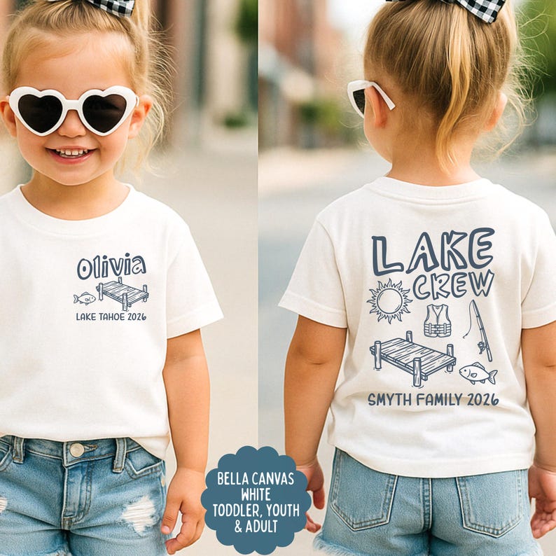 May include: White t-shirt with blue graphic of a dock, fish, and the text "Olivia" and "Lake Tahoe 2026" on the front. The back of the shirt has "Lake Crew" and fishing-themed graphics, with "Smyth Family 2026".