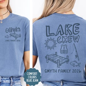 May include: Blue jean-colored t-shirt with the text "Olivia" and "Lake Tahoe 2026" on the front. The back of the shirt says "Lake Crew" with lake-themed graphics and "Smyth Family 2026".