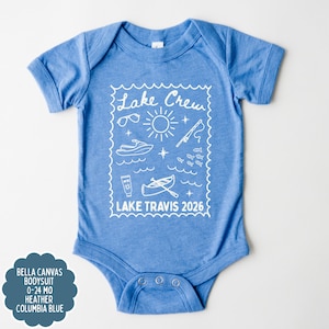 May include: A light blue baby bodysuit with a white graphic that says "Lake Crew" and features sunglasses, a sun, a jet ski, a fishing pole, fish, sunscreen, and a canoe. The text "Lake Travis 2026" is also included.