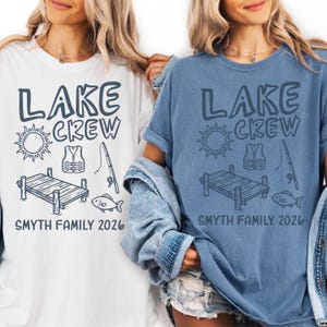 May include: Two t-shirts, one white and one blue, each with a "LAKE CREW" graphic. The graphic includes a sun, life vest, fishing rod, dock, and fish. The text "SMYTH FAMILY 2026" is below the graphic.