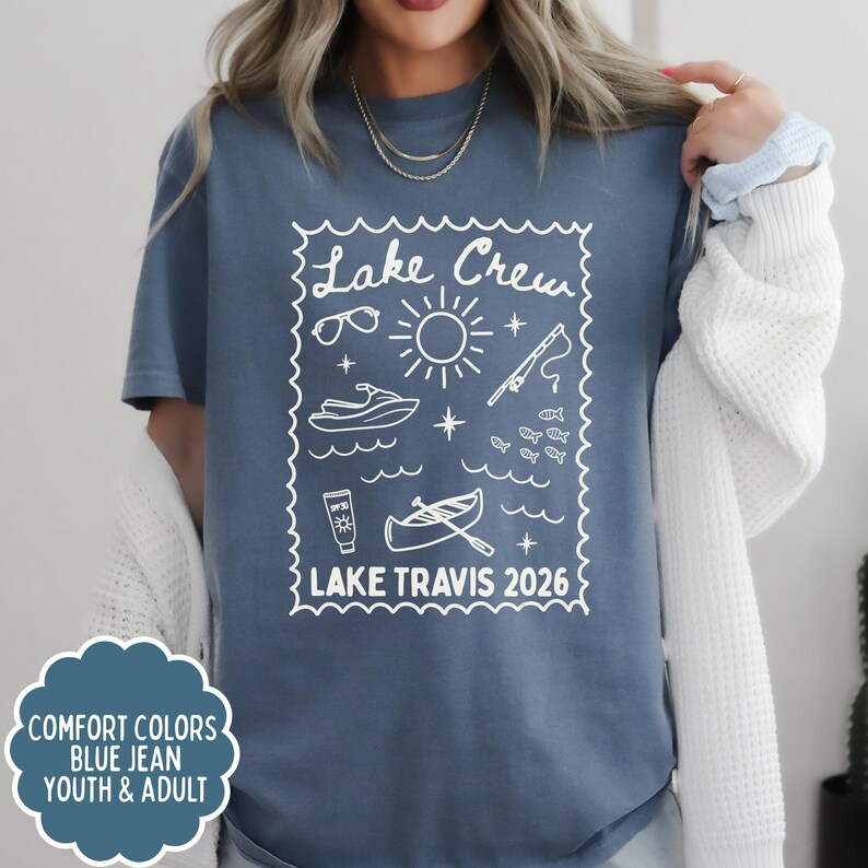 May include: Blue jean-colored t-shirt with a white graphic that reads "Lake Crew" and features sunglasses, a sun, a jet ski, a fishing rod, fish, a boat, and the text "Lake Travis 2026". The shirt is available in youth and adult sizes.