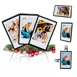 May include: Three black picture frames with white mats, each displaying a different family photo. The frames are arranged in a row, with the middle frame slightly higher than the others. The frames are sitting on a table with a green and red Christmas garland.