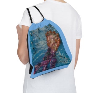 May include: A blue drawstring bag with a black trim and a colourful abstract design featuring a hand with a pink and orange design.