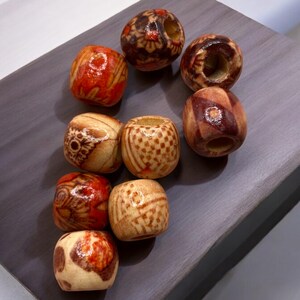 May include: A collection of ten wooden beads with intricate patterns and designs in shades of brown, orange, and red. The beads are round and have a hole in the centre for threading.