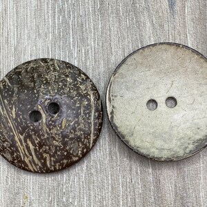 May include: Two coconut shell buttons with two holes each. One button is brown with a natural wood grain pattern. The other button is a light beige colour.