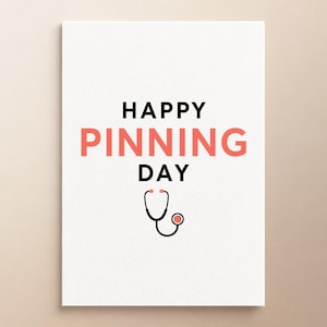 Może przedstawiać: Biała prostokątna kartka z czarnym napisem HAPPY i DAY oraz słowem PINNING w kolorze koralowego różu. Pod tekstem znajduje się prosty czarno-koralowy rysunek liniowy stetoskopu medycznego, wyśrodkowany na białym tle.