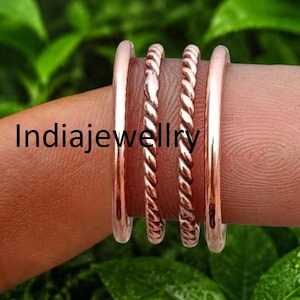 Op de afbeelding: Een set van vier koperkleurige ringen met twee gladde banden aan de buitenranden en twee gedraaide, touwachtige banden in het midden. De tekst Indiajewllry is zichtbaar op de ringen. De ringen zijn van metaal met een gepolijste afwerking.