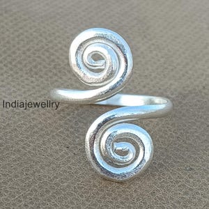 May include: Silver ring with two spiral designs. The ring is adjustable and can be worn on any finger.