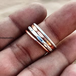 May include: A set of four thin stacking rings in silver and copper. The rings are hammered and have a textured finish.