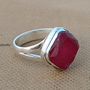 Op de afbeelding: Een zilveren ring met een grote, vierkante, gefacetteerde, rode edelsteen. De ring heeft een eenvoudige band met een gesplitst ontwerp.